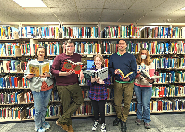 Library staff members holding books in front of bookshelf.